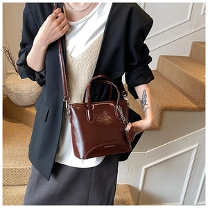 Detail of dark red glossy leather bucket bag with mini chain accessory and long strap