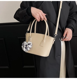 Close-up of beige leather bucket bag with leopard print heart charm on black coat