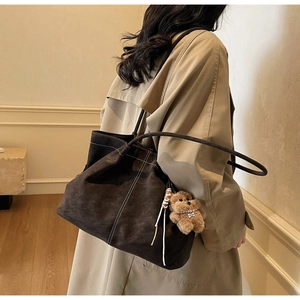 Detail view of large dark brown tote bag with contrast stitching and teddy bear charm