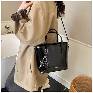 Detail of a black patent leather tote bag with a mini pouch pendant and shoulder strap