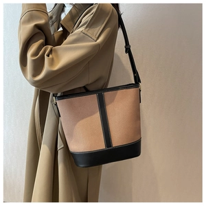 Detail of a brown fabric bucket bag with black leather trim and white contrast stitching