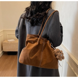 Detail of brown suede tote bag with white contrast stitching and plush bear charm