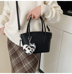 Detail of black textured leather bag with leopard heart charm on adjustable strap