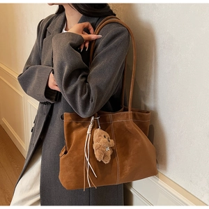 Detail of a brown suede tote bag with woven fringe and a plush bear charm on a model