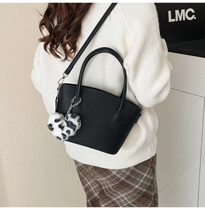 Detail of black lychee grain leather bag with heart leopard print plush pendant charm