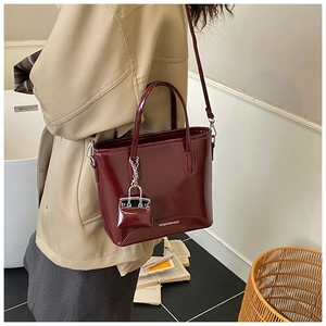 Detail of burgundy glossy patent leather tote bag featuring a decorative mini bag charm