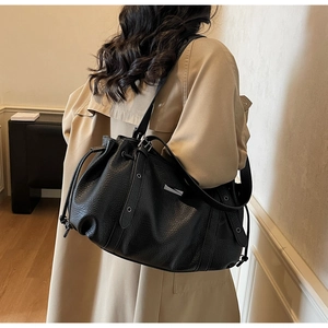 Detailed view of black pebbled leather tote bag with silver eyelets on beige trench coat