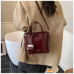 Detailed view of glossy burgundy patent leather bucket bag with silver chain mini charm