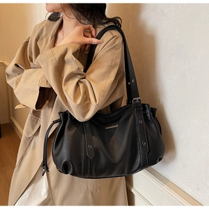 Detail of black litchi texture tote bag with side eyelets and drawstring on khaki coat