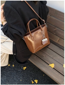 Detail of a shiny brown retro bucket bag with a miniature charm on an outdoor bench