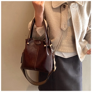 Détail du sac seau en cuir marron foncé avec une large bandoulière à motif vintage