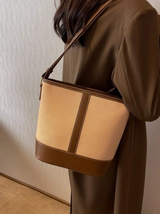 Fashionable canvas and leather bucket bag worn over the shoulder by a model in brown suit
