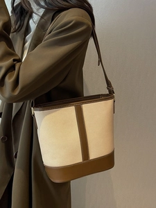 Minimalist canvas bucket bag with brown leather trim shown on shoulder of a model