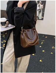 Sac seau en cuir marron avec bandoulière tissée géométrique sur rue parsemée de feuilles