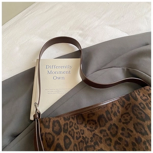 Detailed view of leopard print shoulder bag with brown leather strap on soft fabrics