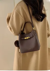 Détail du sac seau en cuir marron foncé avec fermoir doré et breloque sur manteau camel