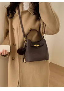 Détail du sac seau marron foncé avec logo doré, fermoir rotatif et pompon en fourrure