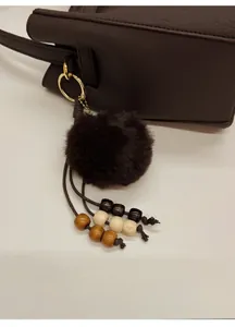 Détail du pendentif en peluche marron avec perles en bois et anneau doré sur sac cuir