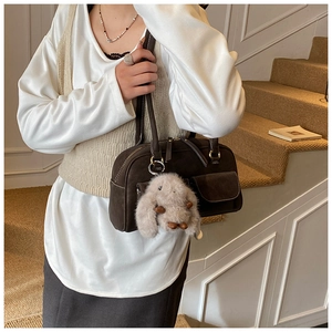 Detail of dark brown suede shoulder bag with a plush rabbit pendant on a staircase