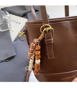Detail of dark brown PU leather bucket bag with artistic wooden bead pendant and metal buckle