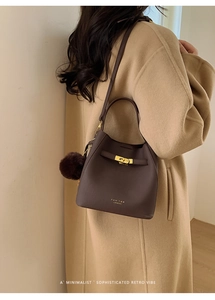 Détail du sac seau en cuir marron avec fermoir doré et pompon sur un manteau en laine