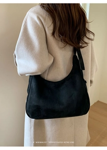 Black hobo bag shown on shoulder over cream coat highlighting the retro minimalist aesthetic