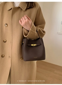 Détail du sac seau en cuir marron foncé avec fermoir doré et logo sur manteau en laine