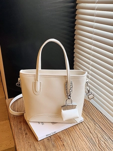 Retro white PU leather bucket bag with top handles and a mini charm on a wooden surface