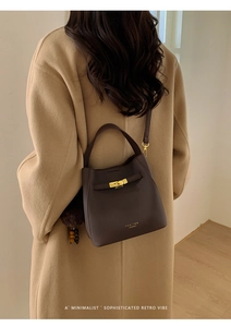 Sac minimaliste en cuir marron foncé avec boucle dorée porté par un mannequin en manteau