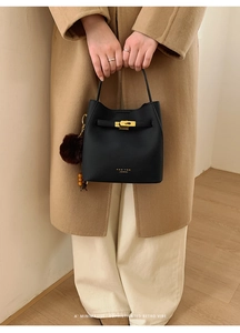 Détail du sac seau noir en cuir avec fermoir doré et pendentif pompon marron doux