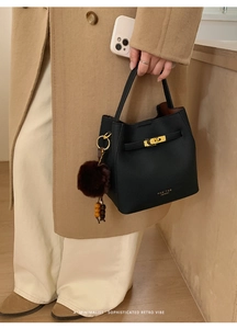 Détail du sac seau en cuir noir avec fermoir doré et breloque sur manteau d'hiver