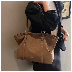Detail view of brown matte leather tote bag with silver metallic rings and buckle straps