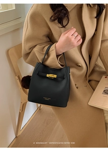 Détail d'un sac à main minimaliste en cuir noir avec boucle dorée sur un manteau en chameau