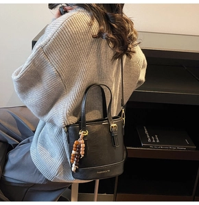 Detail of black leather bucket bag with gold logo, double handles and beaded tassel charm