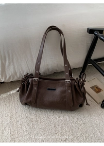Detail of dark brown pebble leather shoulder bag with metallic eyelets and side drawstrings