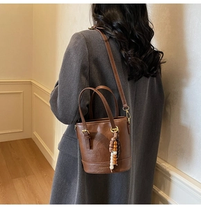 Detail of brown PU leather bucket bag with ethnic beaded charm and gold-tone hardware