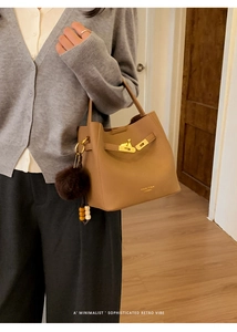 Détail du sac seau en cuir marron avec fermoir doré et un pendentif pompon doux