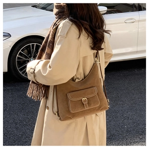 Close-up of a brown suede hobo bag with a buckled front pocket in a street setting