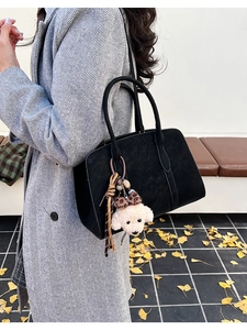 Détail du sac cabas en daim noir avec pendentif ours porté avec un manteau d'hiver