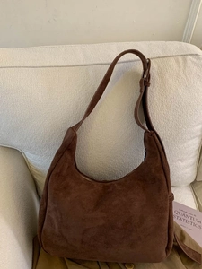 Brown faux suede hobo bag with adjustable strap displayed on a cozy fabric sofa