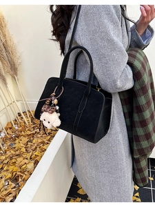 Détail d'un sac à main noir en cuir mat avec un pendentif chiot en peluche sur un manteau
