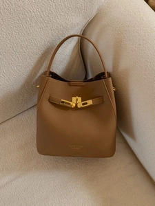 Sac seau chic en cuir caramel sur canapé avec détails dorés et poignée supérieure élégante