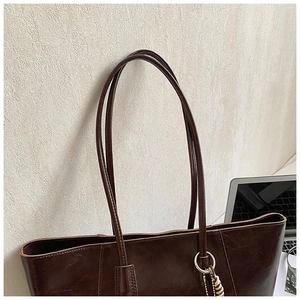 Detail of dark brown tote bag featuring metallic ring and braided charm ornament