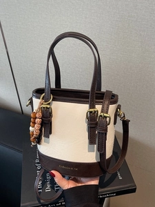 Minimalist bucket bag in beige PU leather with brown contrast trim and wood bead charm