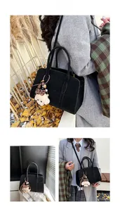 Détail du sac à main en cuir noir avec deux poignées et un charmant petit chien en peluche