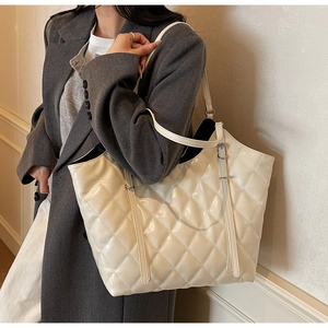Detail of a large cream quilted tote bag with glossy finish on a gray blazer outfit