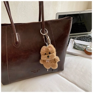 Close-up of brown plush dog charm with TOP DOG tag on a dark brown leather tote bag
