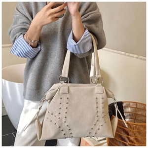 Detailed macro view of beige tote bag featuring metallic stud V-pattern and side tassels