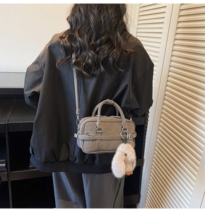 Detail of dark grey handbag with matte finish and white plush bunny charm on shoulder strap