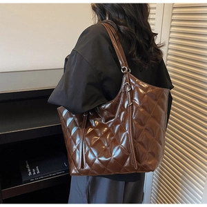 Detail of coffee quilted tote bag in glossy leather worn by a model in a warm indoor setting